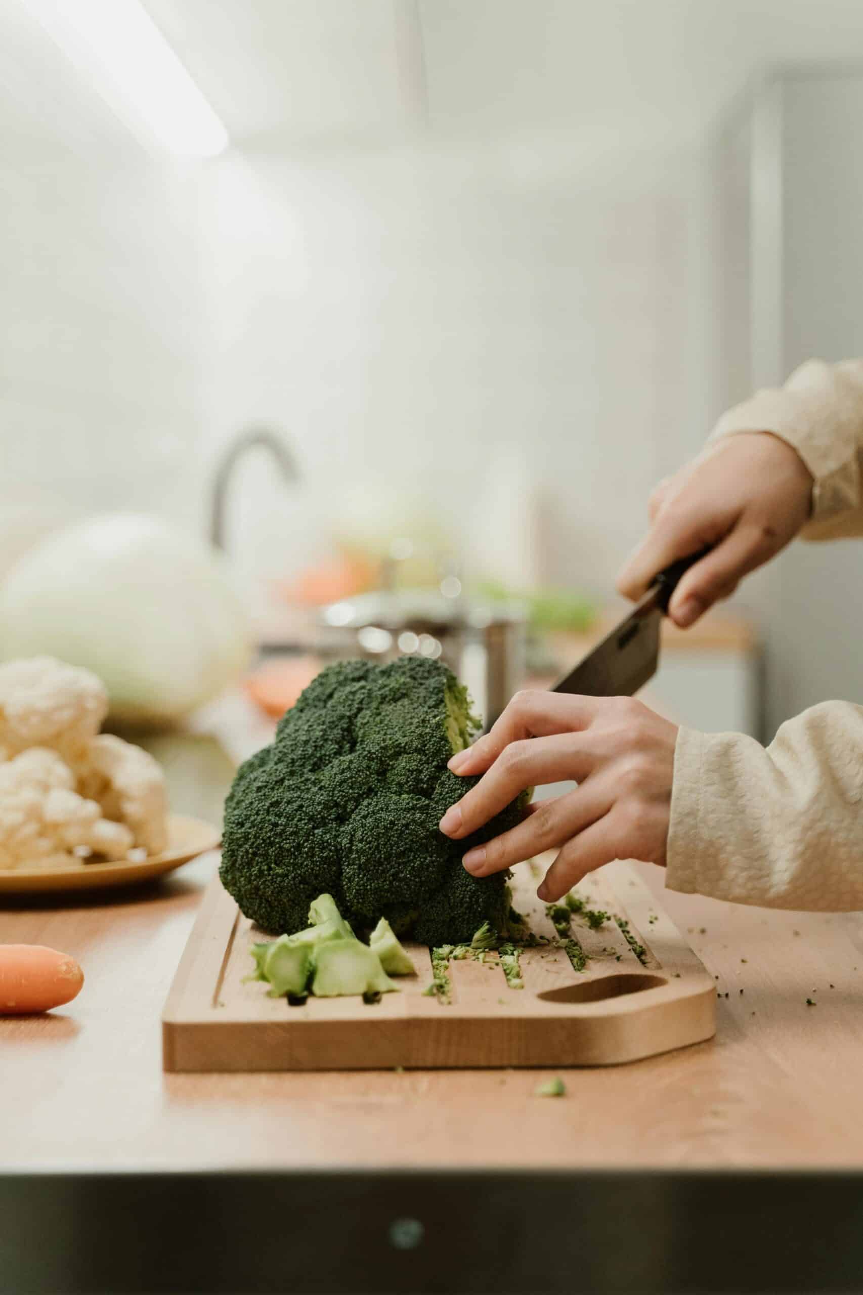 Close-up of hands slicing fresh organic broccoli on a kitchen counter, perfect for food preparation themes.