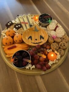 Allergy-friendly spooky charcuterie board with fruit, cookies, rice cakes, popcorn, and Halloween decorations.