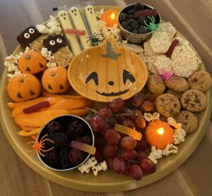 Allergy-friendly spooky charcuterie board with fruit, cookies, rice cakes, popcorn, and Halloween decorations.