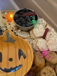 Allergy-friendly spooky charcuterie board with fruit, cookies, rice cakes, popcorn, and Halloween decorations.