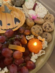 Allergy-friendly spooky charcuterie board with fruit, cookies, rice cakes, popcorn, and Halloween decorations.