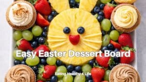 Easy Easter dessert board with fruit bunny made from pineapple, strawberries, grapes, and cupcakes arranged on a platter