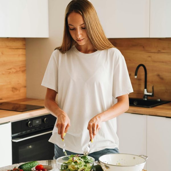 A woman preparing a fresh vegetable salad in a modern kitchen for a healthy lifestyle.